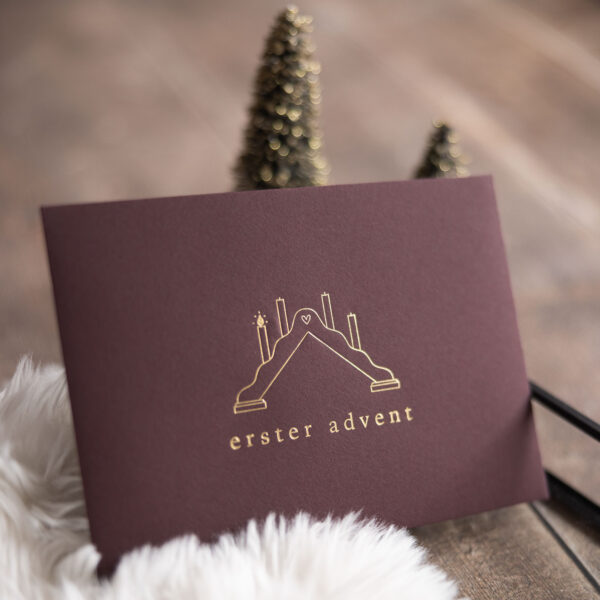 Briefumschlag für einen Adventskalender für vier Adventssonntage, es ist ein geprägter Schwibbogen mit einer angezündeten Kerze zu sehen und darunter die Worte erster Advent, die Prägung ist Gold.