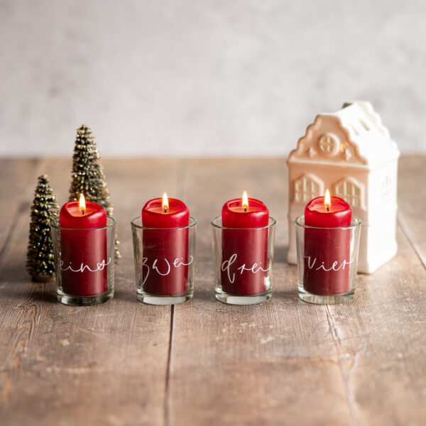 Vier Teelichthalter "Advent" aus Glas, beschriftet mit den Worten eins, zwei, drei und vier.